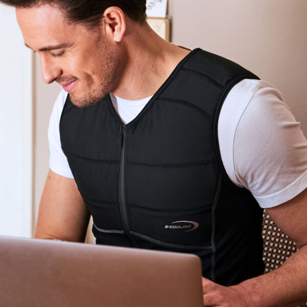Uomo indossa una maglia smanicata refrigerante E.COOLINE di colore nero e lavora al suo computer portatile.